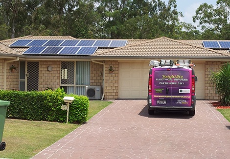 A brightlite electrical van parked in front of a single storey property with solar panels on the roof.